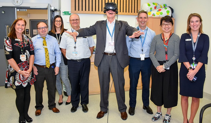man stands with hospital staff in a corridor wearing virtual reality goggles