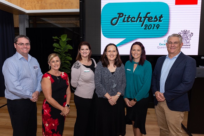 pitchfest review panel stand in front of pitchfest logo on a large digital screen
